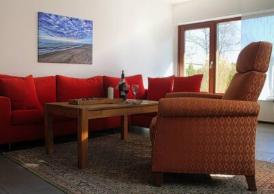 Sitzecke des Wohnzimmers mit Sessel im Vordergrund und rote Couch im Hintergrund